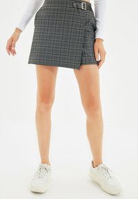 Gray plaid skirt with a wrap design and belted waist. Made from structured fabric, it features a subtle texture and is paired with white sneakers.