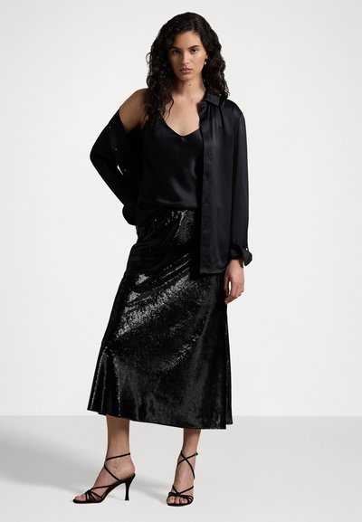 Black satin camisole layered under an open black shirt, paired with a black sequined midi skirt and strappy black heels.