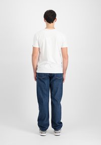 Hvid t-shirt, korte ærmer, afslappet pasform; parret med løse blå denim jeans, let falmede, og detaljer på baglommen.
