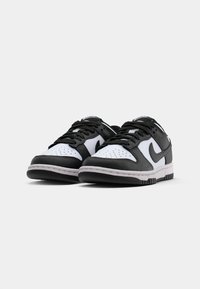 Melnas un baltas ādas tenisa kurpes ar auklām, perforētu purngalu, gumijas zolēm un kontrastējošu Nike swoosh logotipu sānos.