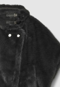 Cloak in finta pelliccia nera con cappuccio, caratterizzato da due fibbie in pelle. Texture morbida, forma arrotondata e un leggero lucido sono dettagli notevoli.