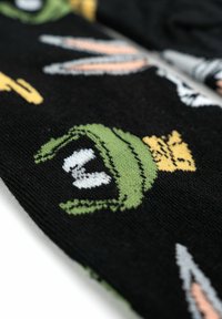 Calze nere lavorate a maglia con un motivo di personaggi dei cartoni animati, prevalentemente in verde e giallo, con accentuazioni bianche ben visibili.
