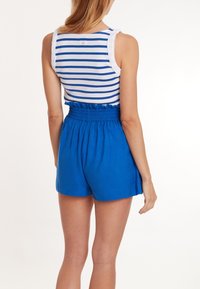 Blaue Shorts mit elastischem Bund und einem figurbetonten, gerafften Design, kombiniert mit einem ärmellosen Oberteil in Weiß und Blau gestreift.