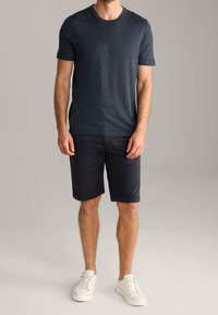 Granatowa koszulka z krótkim rękawem wykonana z teksturowanej tkaniny, zestawiona z czarnymi szortami i białymi trampkami. Prosty, swobodny design.