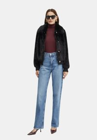 Bomber jacket in pelliccia sintetica nera con colletto, indossato sopra un dolcevita bordeaux e jeans a vita alta di colore azzurro chiaro. Modella accessoriate con occhiali da sole.