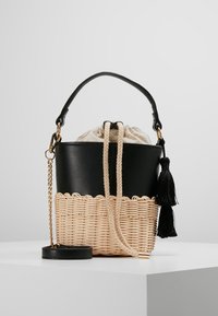 Czarna torba typu bucket z faux skóry z plecioną beżową podstawą, zapięciem na sznurek, czarnym akcentem w postaci frędzli oraz złotą łańcuszkową rączką.
