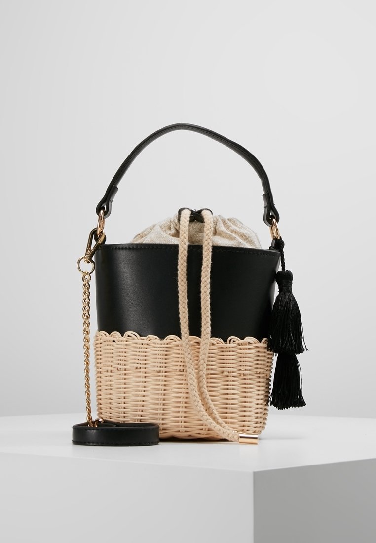 Czarna torba typu bucket z faux skóry z plecioną beżową podstawą, zapięciem na sznurek, czarnym akcentem w postaci frędzli oraz złotą łańcuszkową rączką.