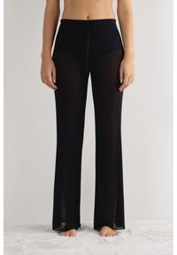 Zwarte geribbelde gebreide broek met een tailleband met trekkoord; voorzien van doorzichtig materiaal, wijde pijpen en zijsplitten bij de zoom.