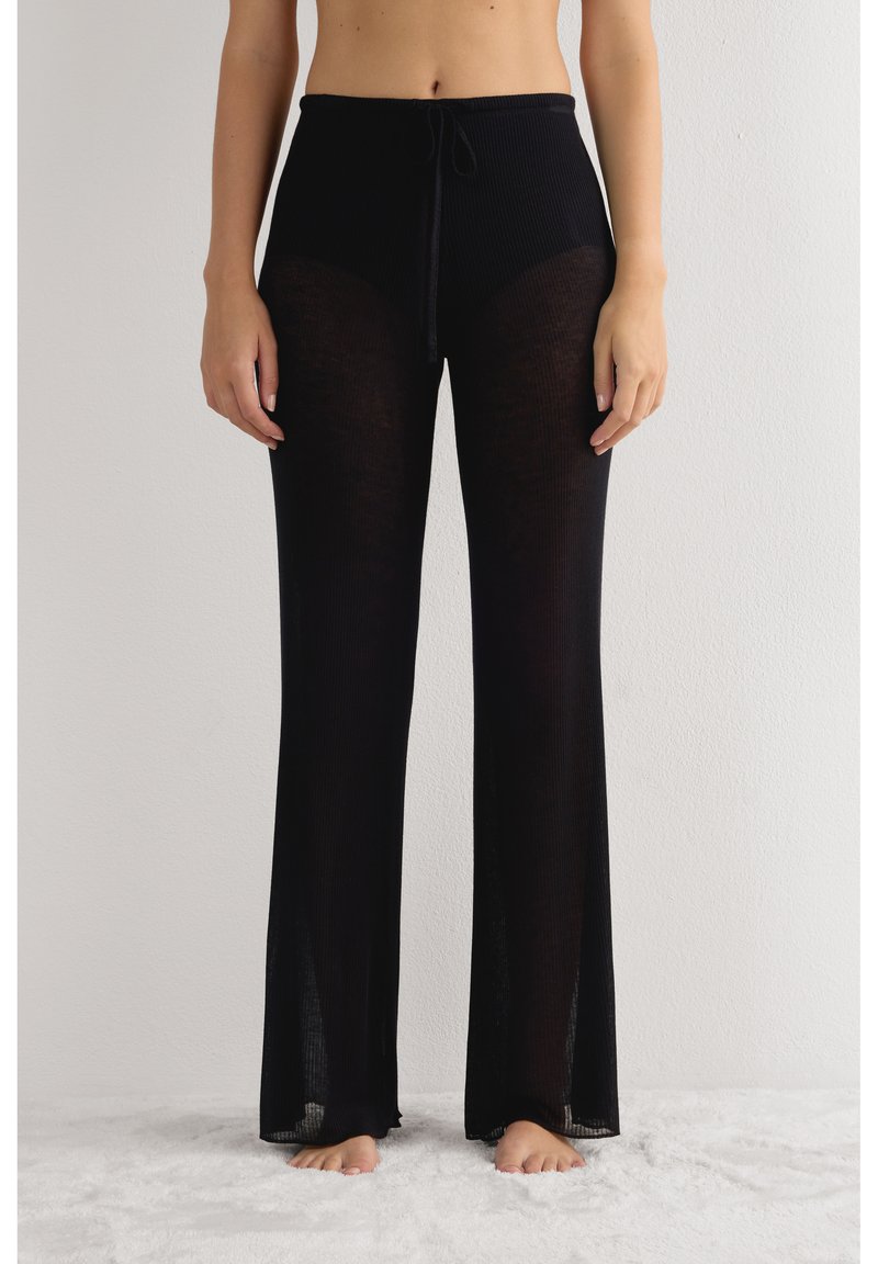 Zwarte geribbelde gebreide broek met een tailleband met trekkoord; voorzien van doorzichtig materiaal, wijde pijpen en zijsplitten bij de zoom.