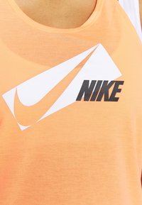 Canotta in cotone arancione con un grande logo Swoosh Nike bianco e nero e testo. Tessuto morbido con scollo a barco.