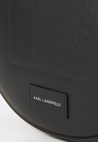 Borsa in pelle nera con una texture liscia, forma arrotondata e un'etichetta rettangolare con "KARL LAGERFELD" impresso in bianco.