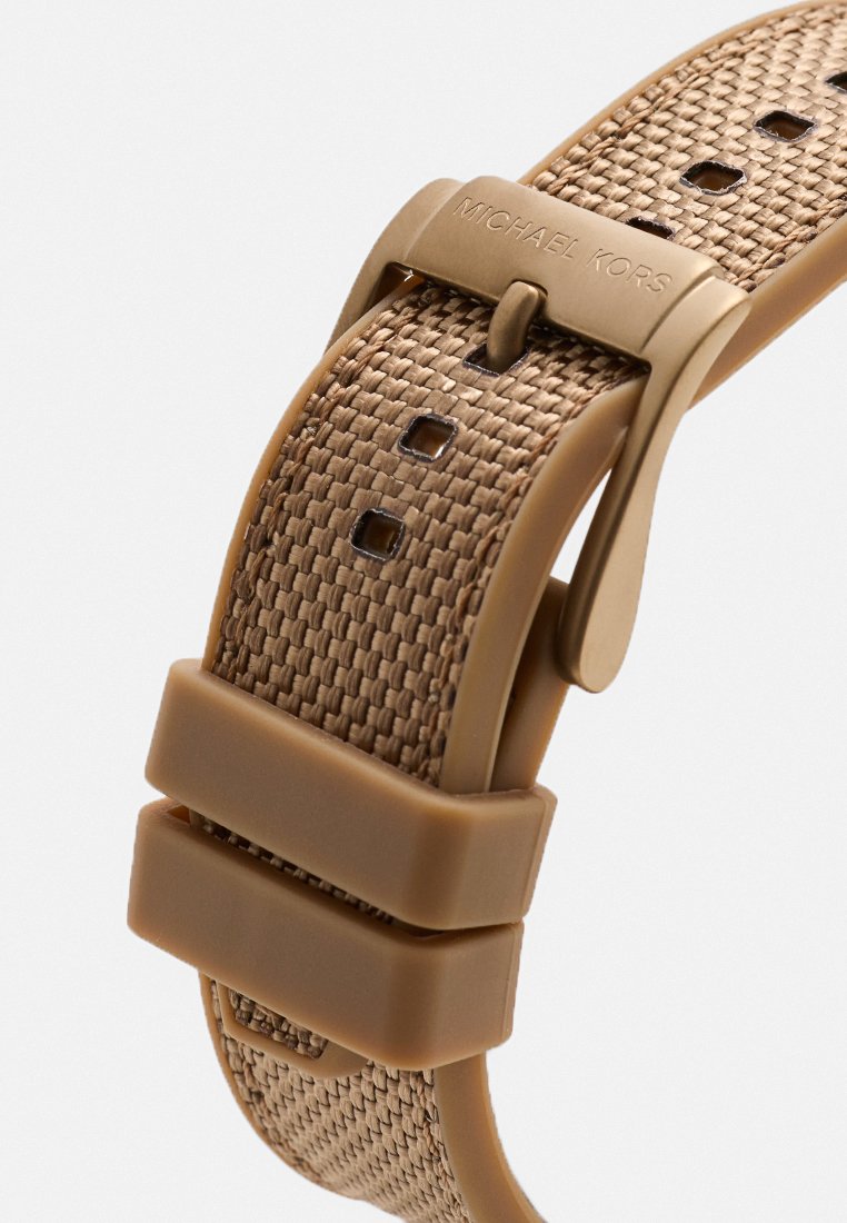 Bracelet de montre en nylon tissé marron avec une finition mate, doté d'une boucle en métal et de plusieurs trous de réglage pour un ajustement parfait. Détail du logo bien visible.