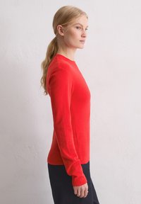 Czerwona koszula z długim rękawem wykonana z miękkiego materiału, z okrągłym dekoltem i dopasowanym krojem, w połączeniu z ciemnymi spodniami.