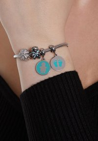Armband aus Sterlingsilber mit mehreren Anhängern: eine Blume mit Kristallen, ein Bär und zwei Scheiben in Teal mit einer Figur und Fußabdrücken.