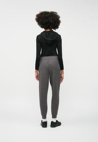 Svart långärmad hoodie med huva, kombinerad med grå joggerbyxor som har elastiskt midjeband och ribbade manschetter, bärs med svarta sneakers.