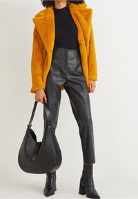 Cappotto in pelliccia sintetica gialla, maglione a coste nero, pantaloni di pelle neri a vita alta, stivaletti neri con tacco e una grande borsa a tracolla nera.