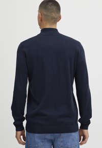 Pull en laine bleu marine avec un col montant, des manches longues et des poignets et un ourlet côtelés. Texture lisse, design minimaliste.