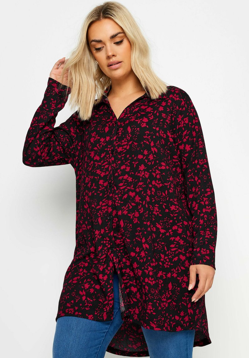 Svart knapplång blus med röd blommönster, långa ärmar och en något rundad nederkant. Har en krage och textil med struktur.