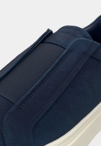 Baskets à enfiler en daim bleu marine avec panneau élastique, semelle en caoutchouc blanche et accents cousus. Vue en gros plan mettant en valeur la texture et le design.