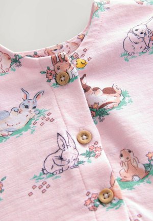 Rosa Stoffbluse mit Kaninchen- und Blumenmotiven, ausgestattet mit Holzknöpfen und einem Rundhalsausschnitt. Weicher Stoff, verspieltes Design.
