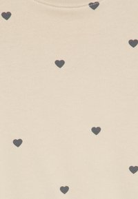Pull crème, avec une texture douce, orné de motifs de cœurs noirs dispersés. Encolure ronde simple, en tissu tricoté.