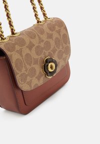 Borsa a mano in pelle marrone e tela monogram con manici a catena dorati e chiusura a scatto a forma di fiore in oro e nero.