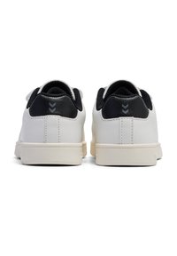 Vita sneakers med svart läderhälek, strukturerad yta och neutral gummisula. Har sömdetaljer och en chevron-accent på hälen.