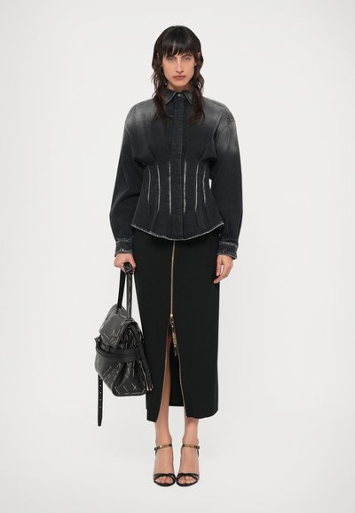 Camicia nera in denim a corsetto con una finitura sbiadita, abbinata a una gonna midi nera con zip frontale. Borsa a spalla nera e tacchi.