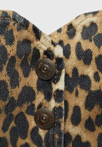 Látka s leopardím potiskem s hnědými a černými skvrnami, která má dva tmavé kovové patentky s vyrytým textem na prošívaném materiálu.