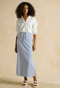 Biała bluzka z długim rękawem i dekoltem w serek, zestawiona z pasiastą, niebiesko-białą spódnicą maxi z wiązaniem w talii i bocznym rozcięciem.