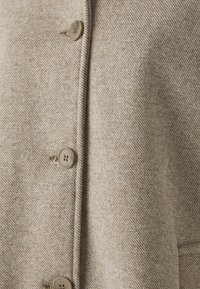 Lichtbeige wollen jas met diagonale weefstructuur, voorzien van ronde beige knopen en zichtbare knoopsgaten op de voorflap.