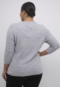 Pull gris texturé avec manches trois-quarts et col rond. Le tissu semble doux, avec une finition lisse et un motif subtil.