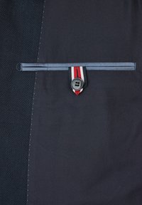 Marineblauer Stoff mit einem strukturierten Muster, ausgestattet mit einem Knopf und einem Riemen, der einen rot-weiß-blauen Streifen aufweist. Strukturiertes Design mit kontrastierenden Elementen.