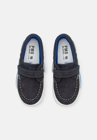 Scarpe slip-on blu navy con dettagli bianchi, soletta imbottita e cinturino con velcro. Presenta un accento azzurro sul tallone.
