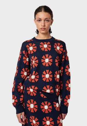 Knitted sweater in navy blue featuring a floral pattern with orange petals and white centers. Ribbed neckline and cuffs. Textured fabric.