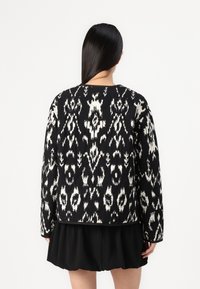 Casaco com padrão em preto e branco, de mangas longas e decote redondo, apresentando um intricado design ikat e um tecido ligeiramente texturizado.