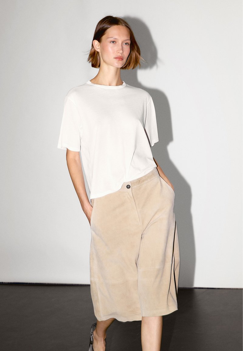 Witte katoenen T-shirt met korte mouwen, gecombineerd met beige suède culottes met een sluiting aan de voorkant en zijzakken.