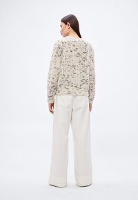 Grober, cremefarbener Strickpullover mit grauen Sprenkeln, einem runden Ausschnitt und geripptem Muster, kombiniert mit weißen, weit geschnittenen Hosen.