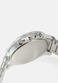 Silberner Edelstahl-Uhr mit einer strukturierten Krone, zwei Drückern und einem polierten Armband, das ein minimalistisches Gehäuse und einen glatten Rücken aufweist.