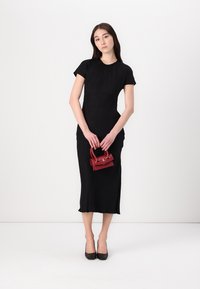 Black, short-sleeve dress with a fitted silhouette and midi length. Features a textured fabric and a round neckline, paired with a small red handbag.