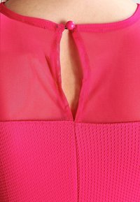 Fuchsian rosa topp med en texturerad kropp, genomskinlig halsringning och en knäppning på baksidan. Slät tyg med en lager-på-lager, öppen ryggdesign.