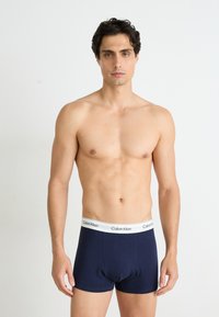 Marineblå bomullsboxer med hvit elastisk midjebånd preget med "Calvin Klein"-logo, tettsittende design og glatt tekstur.
