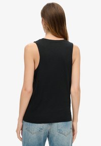 Zwarte mouwloze tanktop van zachte stof, met een relaxte pasvorm en ronde halslijn; gedragen met vervaagde blauwe denim jeans.