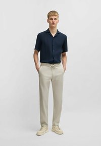 Navy short-sleeve button-up shirt, beige drawstring trousers, and cream sneakers. Fabric appears lightweight; shirt has a collared neckline.