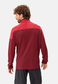 Pullover bordeaux con colletto alto, caratterizzato da un corpo testurizzato e pannelli spalle lisci. Maniche lunghe con forellini per il pollice, design minimalista.