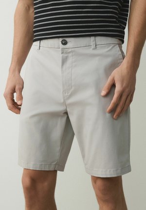 Mann trägt hellgraue knielange Shorts und ein schwarz-weiß gestreiftes Hemd, steht mit entspannten Händen an den Seiten.