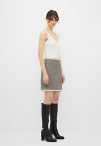 Top blanco sin mangas con escote en V, combinado con una falda marrón con estampado. El modelo lleva botas de tacón altas negras con acentos dorados.