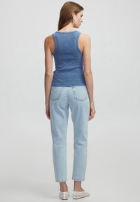 Niebieski prążkowany top na ramiączkach w połączeniu z jasnoniebieskimi dżinsami z wysokim stanem oraz białymi butami na slip-on. Widok z tyłu pokazuje dopasowany krój i fakturowany materiał.