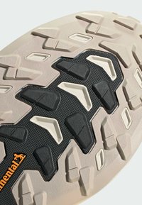 Semelle de chaussure beige avec une bande de roulement en caoutchouc texturé noir et blanc présentant des formes géométriques et un petit logo Continental orange.