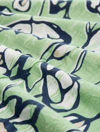Grüner Stoff mit abstrakten Mustern in Marineblau und Weiß sowie einer subtilen Textur. Das Design umfasst geschwungene Formen und fließende Linien.